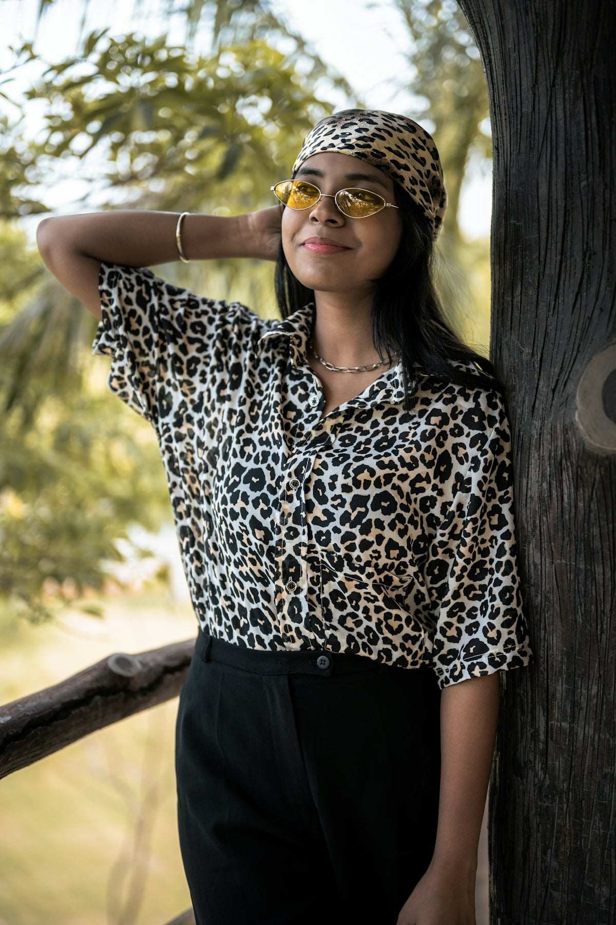 A woman leaning against a tree wearing sunglasses