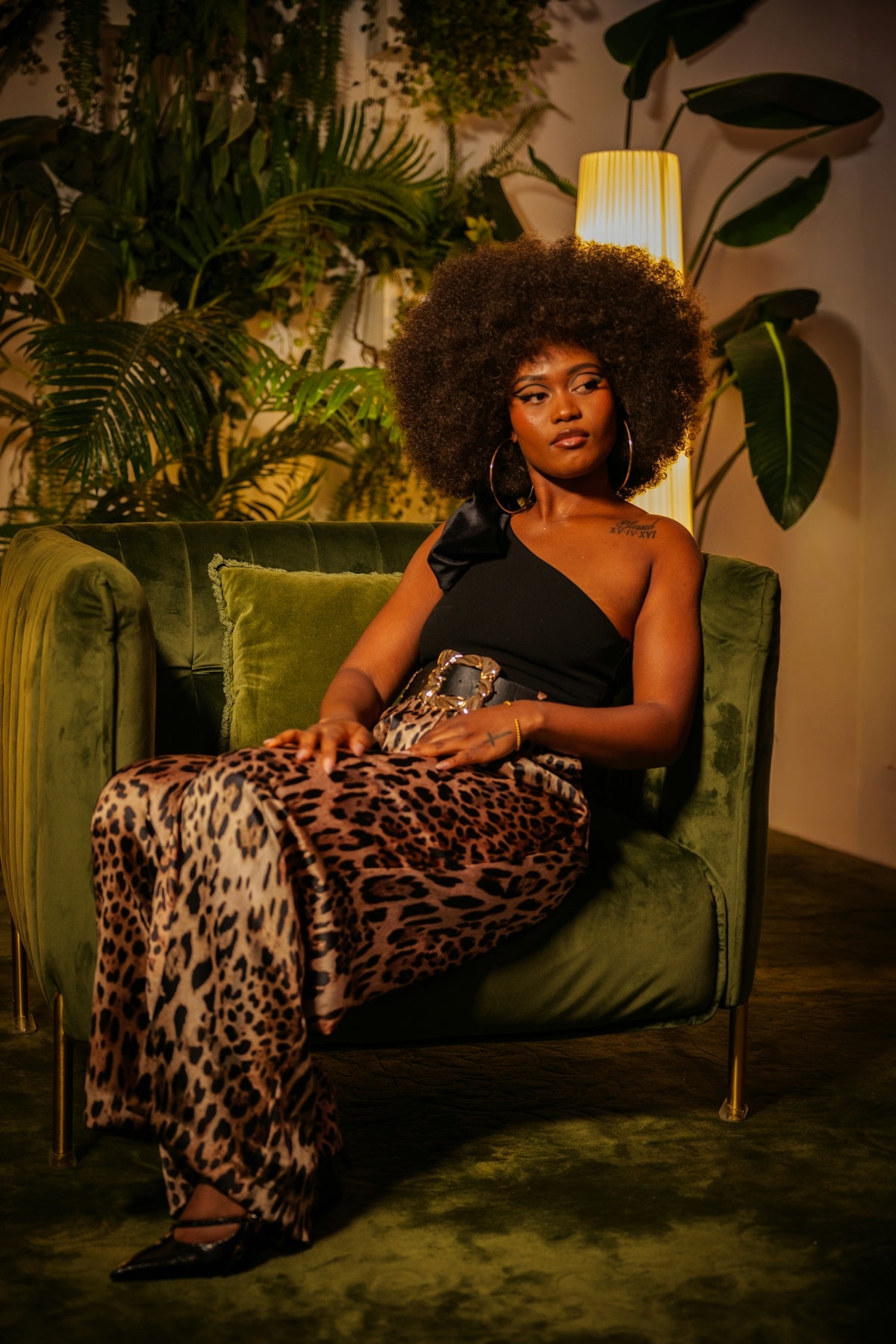 Woman with afro hairstyle sits in a velvet armchair.