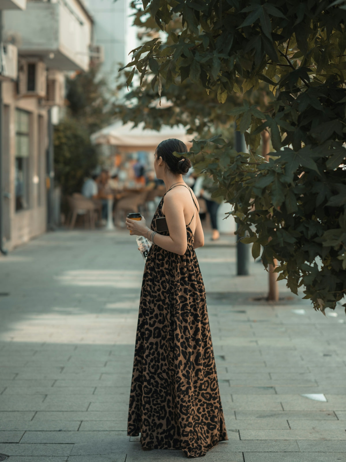 Woman in leopard print dress holding coffee cup on street